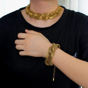 Close-up of golden woven mesh necklace and bracelet set worn by a model against white curtain