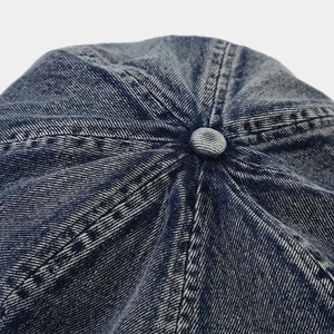 Macro view showing six-panel stitching and top button of washed denim newsboy cap