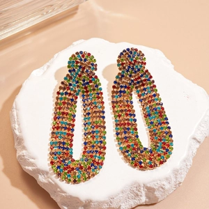 Macro view of long oval gold earrings with colorful rhinestones on a white pedestal