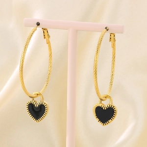 Detail of gold twisted hoop earrings with black heart charms on a pink jewelry stand