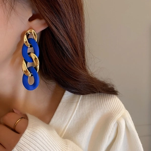 Close-up of geometric chain earrings with gold metal and matte Klein blue rings