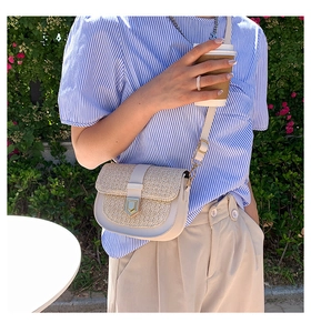 Detail of a beige woven straw saddle bag with gold metal buckle on a shoulder strap