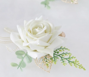 Detailed close-up of cream boutonniere with golden metal leaves and green foliage