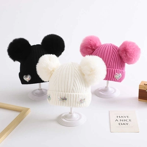 Three knit baby hats in black, pink, and white with double pom-poms and sequined hearts