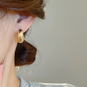 Dettaglio dell'orecchino a goccia in metallo dorato minimalista indossato da una modella