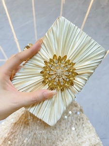 Nahaufnahme der eleganten Plissee-Seidenkupplung mit funkelnder Sonnenblumen-Strassbrosche