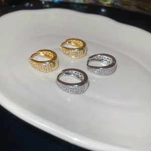 Detail of gold and silver U-shaped earrings with micro-set zircon on white ceramic plate