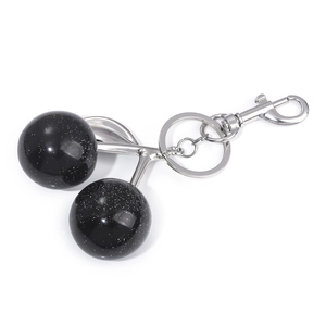 Detail of cherry keychain with glossy black resin beads and silver metallic leaf charm