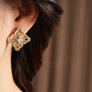 Detail of gold hollow floral stud earring with sparkling zircons worn by a model