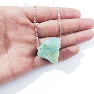 Macro shot of light green raw crystal stone pendant held in hand on silver chain