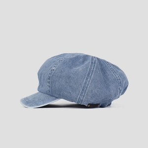 Detailed side view of a light blue washed denim newsboy cap with white contrast stitching