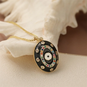 Collier en chaîne dorée avec pendentif ovale noir motif mauvais œil posé sur un coquillage