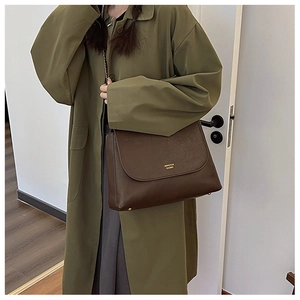 Detailed view of brown crossbody bag with gold hardware worn with green trench coat