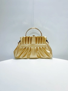 Detail of gold pleated evening clutch featuring a round metal handle and textured finish