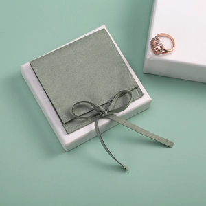 Detail of sage green velvet jewelry pouch with bow on a white gift box with rose gold ring