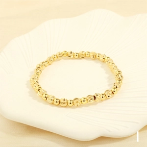 Close-up of golden beaded bracelet with faceted beads on a ceramic scallop plate