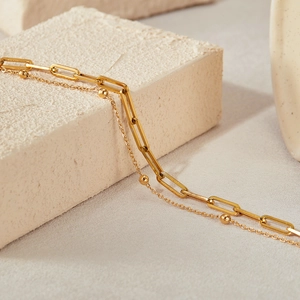 Detailed close-up of a double-layered gold paperclip and satellite chain bracelet