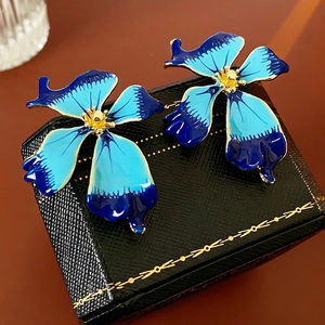 Vintage blue enamel flower stud earrings with gold trim on a black jewelry box