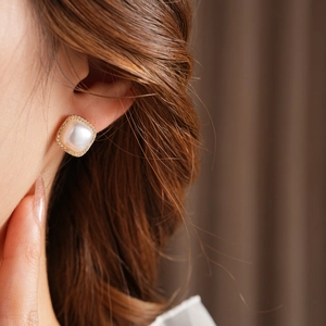 Macro shot of gold plated square zircon pearl earring worn by model on earlobe
