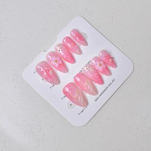 Detail of almond press-on nails with 3D flowers, gradient pink finish, and butterfly art