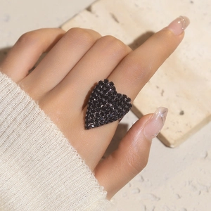 Detailed view of a large black heart-shaped ring with pavé crystals on a model's finger
