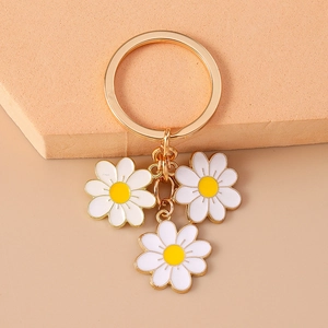 Golden keychain with three white daisy enamel pendants on a minimalist wooden display