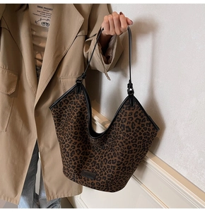 Detail of leopard print tote bag with black leather handles held by a model in a trench coat
