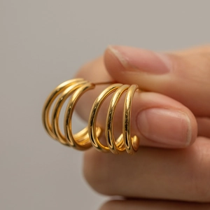 Close-up of triple-layered 18K gold plated stainless steel hoop earrings held by hand