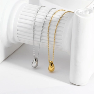 Minimalist gold and silver teardrop pendant necklaces on white columns in a studio setting