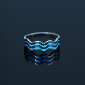 Macro view of wave-shaped stainless steel ring with blue luminous inlay on black surface