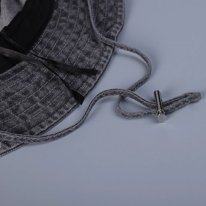 Detail of denim sun hat showing gray fabric texture, white stitching and metal drawstring buckle