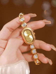 Close-up of a gold oval quartz watch with crystal-encrusted links on a woman wrist