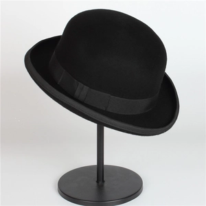 Close-up of a black wool bowler hat featuring a curled brim and ribbon on a metal stand