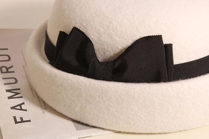 Dettaglio dell'elegante fiocco in gros-grain nero su un cappello cloche in feltro di lana crema