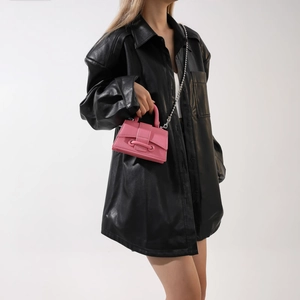 Pink mini leather handbag with silver chain strap shown on a model in a black leather shirt