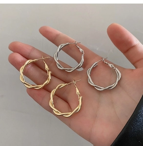 Macro shot of twisted silver and gold hoop earrings held to show texture and size