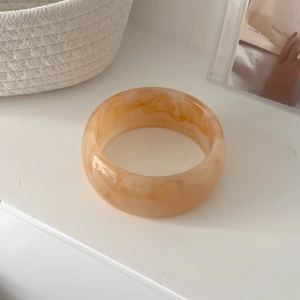 Minimalist wide geometric resin bangle with amber peach marble pattern on white desk