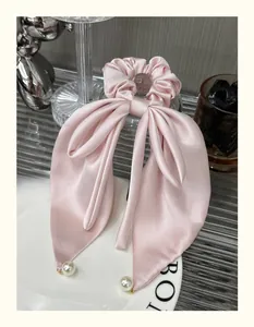 Detail view of a pink satin bow scrunchie with elegant hanging pearl pendant accents
