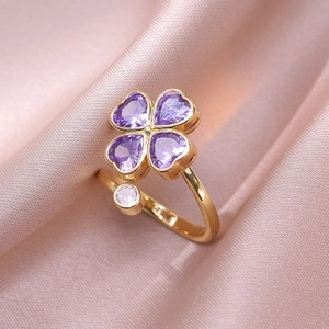 Detail eines Kleeblatt-Rings mit lila Herzsteinen und einem weißen Stein auf rosa Seide