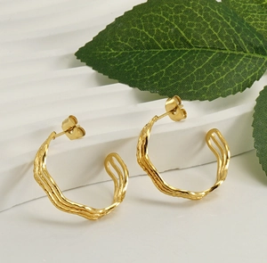 Detailed macro shot of gold C-shaped twisted earrings on a white textured stand