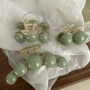 Three green hair claws in different sizes placed on white paper and a wooden table