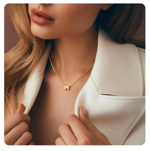 Golden necklace featuring a bubble-style letter M pendant on a model with white jacket