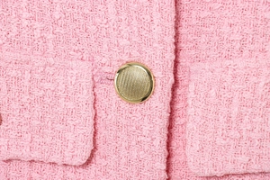 Close-up of pink tweed fabric texture with a decorative gold textured metal button