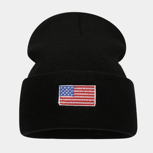 Detail of black knit beanie featuring a stitched American flag patch on a white background