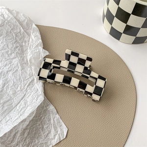 Detail view of the black and white checkerboard hair claw clip on a leather mat
