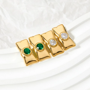Golden bow-shaped stud earrings with green and clear zircon stones on a white stand