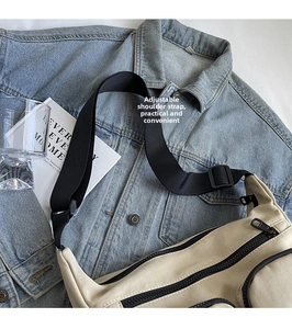 Detail of beige canvas crossbody bag featuring adjustable black strap and multi-pocket design