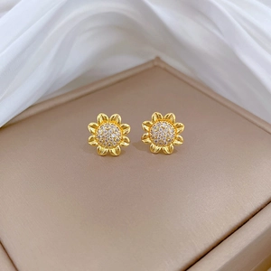 Macro shot of gold sunflower stud earrings with crystals on a beige leather surface