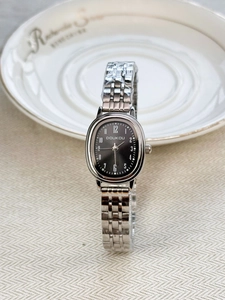 Detail view of oval silver watch with black dial and protective film on metal band
