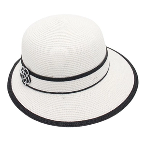 Detail of white woven straw sun hat featuring a black ribbon and camellia flower ornament